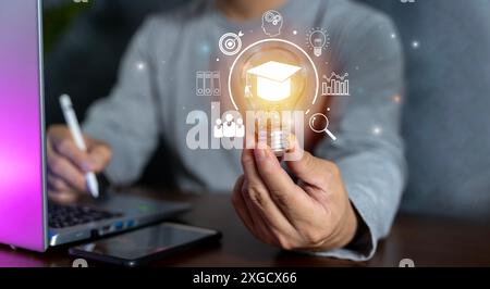 Hand mit Graduierungshutensymbol in der Glühlampe. Internetpädagogik Studienabschluss und Studienwissen. Kreatives Denken mit Ziel, Laptop, Freund Stockfoto