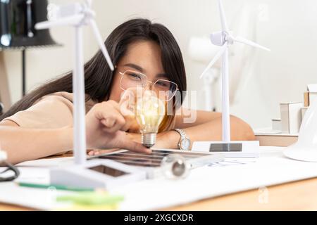 Die Frau hält eine Glühbirne und schaut auf das Licht, während sie über natürliche Energietechnik in inspirierendem Design und Fantasie in der Technologie nachdenkt. Stockfoto