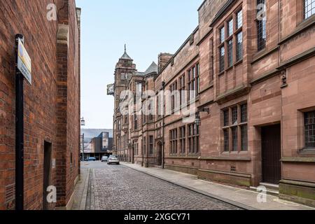 Eine Kopfsteinpflasterstraße führt entlang der Seite des Rathauses von Coventry und des Stadthauses zum Uhrenturm mit seiner kunstvollen goldenen Uhr. Stockfoto