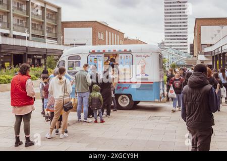 Die Leute stehen geduldig in der Schlange, um ein Eis aus einem Eiswagen in einem städtischen Einkaufszentrum zu kaufen. Stockfoto