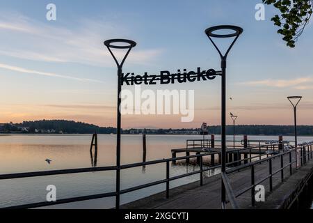 In Waren an der Müritz, Deutschland, erstreckt sich bei Sonnenaufgang der Holzpfeiler Kietz Bruecke mit Geländer in das ruhige Wasser des Sees Stockfoto