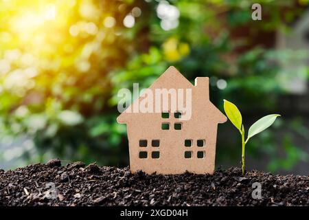 Ein Holzhaus mit Herz und grünen Blättern auf der schwarzen Erde. Investitionen in Immobilien, Grundstücke, Gebäude Konzept. Das Hausmodell befindet sich auf dem Stockfoto