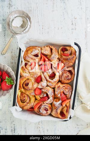 Erdbeerrollies Blätterteig mit Pudding innen und mit Puderzucker bestreut auf weißen rustikalen Holztisch. Rezeptidee für das Sommerfrühstück. Abdeckung Stockfoto