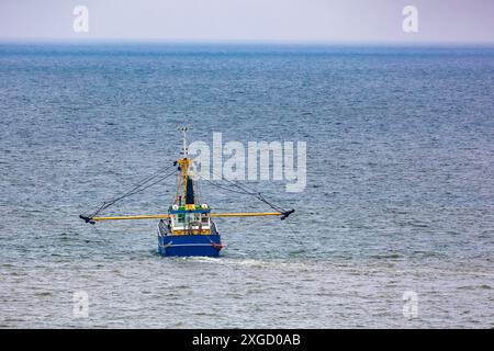 Ein kleines blau-gelbes Fischerboot mit gelben Stützen für Drachen, die von hinten auf einem ruhigen Meer gesehen werden. Stockfoto