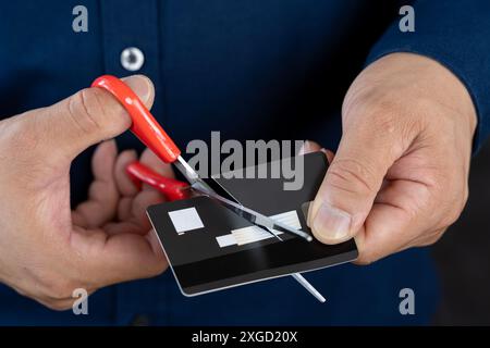 Nahaufnahme der Hände eines Geschäftsmannes, der eine Kreditkarte mit einer Schere schneidet. Geschäftsmann schneidet Kreditkarte, Konkurs-Konzept. Stockfoto