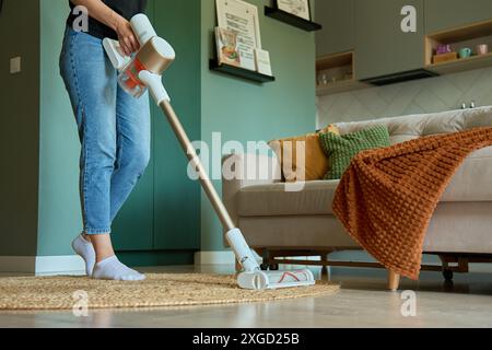 Frau saugt den Boden eines modernen Wohnzimmers mit tragbarem schnurlosem Staubsauger. Tägliche Routine und Hausaufgaben Stockfoto