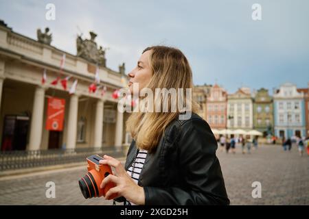 Frau, die Fotos mit orangefarbener Sofortkamera macht. Touristen halten Erinnerungen während der Reise mit einer alten Kamera fest. Weibliche Spaziergänge durch die Stadtstraße Stockfoto