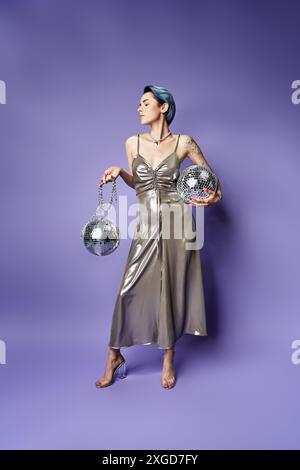 Eine junge Frau mit kurzen blauen Haaren posiert in einem atemberaubenden silbernen Kleid, während sie zwei glitzernde Silberkugeln hält. Stockfoto