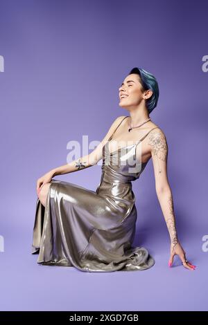 Junge Frau mit kurzen blauen Haaren, die in einem atemberaubenden silbernen Kleid auf dem Boden posiert. Stockfoto