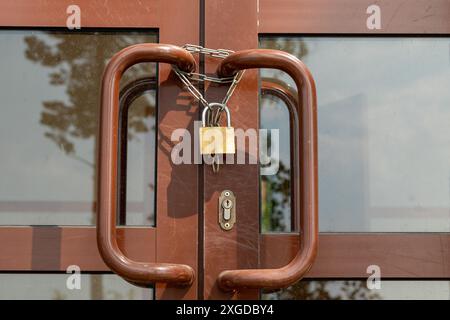 Eine rustikale braune Holztür mit einem altvergoldeten Vorhängeschloss und einer Kette, die an einer alten Gebäudefassade angebracht ist. Komplizierte Details und Glasfenster tragen zu seinem Charme bei Stockfoto