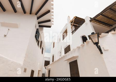Die wunderschöne Stadt Binibeca auf Menorca. Enge Gassen und weiße Wände von Häusern mit Holzelementen, mediterrane Architektur in Spanien Stockfoto