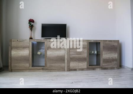 Komfortable, moderne Garderobe. Zwei hellbraune Kommoden mit transparentem Glas, darauf befindet sich ein Fernseher, eine Vase mit einer roten Blume. Stockfoto