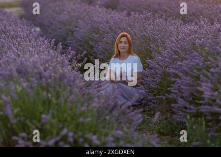 Eine Frau sitzt auf einem Feld mit Lavendelblumen Stockfoto