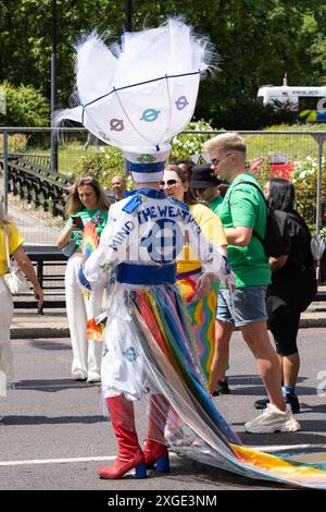 Eine Person, die ein farbenfrohes Kostüm mit einem ausgeklügelten Kopfschmuck, Stiefeln und einem Statement „Mind the Weather“ trägt, repräsentiert TFL beim London Pride 2024 Stockfoto