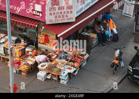 In Chinatown, New York City, stellt ein Lebensmittelhändler sein Obst und Gemüse auf der Straße vor, während ein Lieferfahrer in der Nähe mit seinem Fahrrad und Hi-Vis wartet Stockfoto