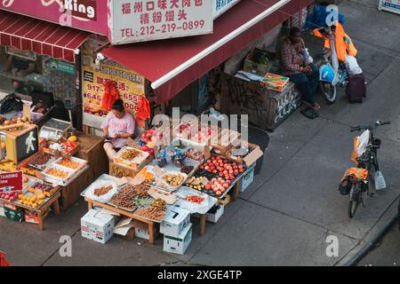 In Chinatown, New York City, stellt ein Lebensmittelhändler sein Obst und Gemüse auf der Straße aus, während ein Lieferfahrer in der Nähe mit seinem Fahrrad wartet Stockfoto