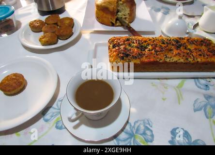 Joghurtbrot aus Haferbrei, Bananenkuchen auf einem weißen Teller, Tasse mit Kaffee und Milch, Panettone, Messer, Butterschale runden den Couchtisch ab. Stockfoto
