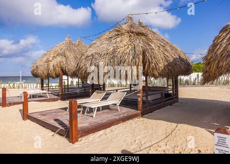 Nahaufnahme einer mit Palmblättern bedeckten Cabana am hoteleigenen Sandstrand mit Liegestühlen, Liegestühlen und Getränketisch. Curacao. Willemstad. Stockfoto