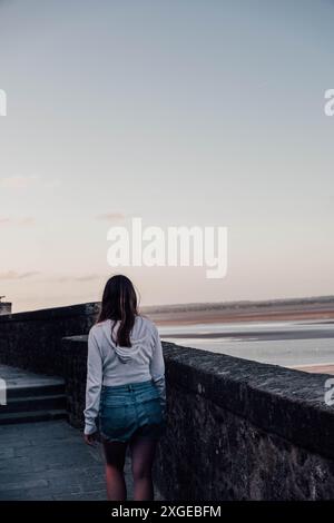 Eine junge Frau, die bei Sonnenuntergang am Meer entlang spaziert. Normandie, Frankreich Stockfoto