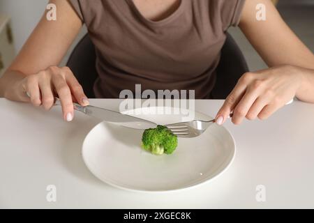 Essstörung. Frau hält Besteck in der Nähe von Brokkoli an einem weißen Tisch drinnen, Nahaufnahme Stockfoto