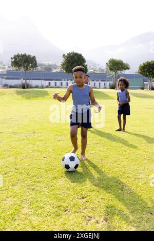 Glückliche afroamerikanische Schulkinder spielen Fußball auf dem Schulfeld Stockfoto