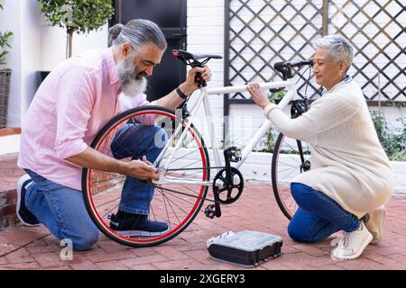 Fahrradreparatur zusammen, Seniorenpaar, das Outdoor-Aktivitäten im Innenhof genießt Stockfoto