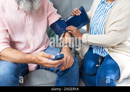Blutdruckkontrolle, Frau, die einem älteren Mann mit einem medizinischen Gerät auf der Couch hilft Stockfoto