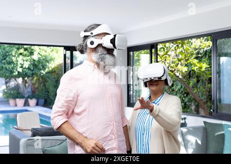 Seniorenpaar, das VR-Headsets nutzt, um die virtuelle Realität im Wohnzimmer zu erkunden Stockfoto