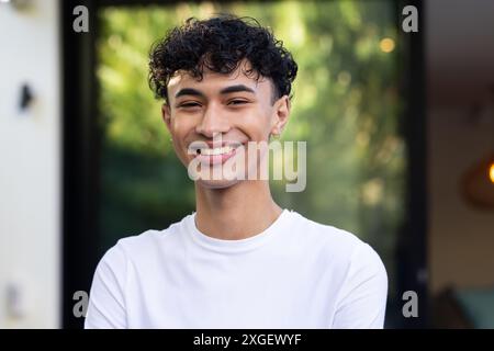 Ein lächelnder junger Mann in weißem Hemd, der vor dem Haus steht und glücklich aussieht Stockfoto
