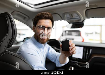 Geschäftsmann, der das Auto kauft, sitzt im Händlerbetrieb und zeigt den Autoschlüssel Stockfoto