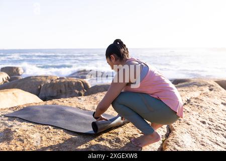 Yoga-Matte aufrollen, Frau beendet Outdoor-Yoga-Session am felsigen Strand, Kopierraum Stockfoto