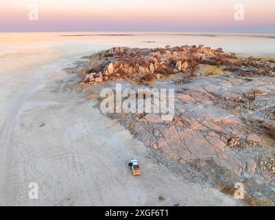 Felsige Insel mit Baobab-Bäumen in einer trockenen Salzpfanne, bei Sonnenuntergang, Geländefahrzeug auf der Salzpfanne, Blick aus der Vogelperspektive, Kubu Island, Botswana Stockfoto