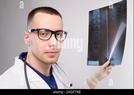 Der junge Radiologe des kaukasischen Arztes hält ein Röntgenbild in der Hand und schaut in die Kamera. Ein Mann in Brille und Uniform mit Stethoskop Stockfoto