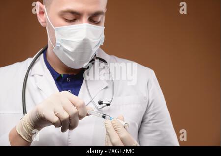 Ein junger weißer kaukasischer Arzt in einem Mantel und einer Maske nimmt einen Impfstoff aus einer Ampulle in eine Spritze. Konzentrieren Sie sich auf die Spritze Stockfoto