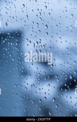 Tropfen Regen auf blauem Glas mit unscharfen Straßen. Abstrakter urbaner Hintergrund Stockfoto