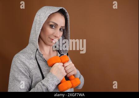 Weibliche Trainerin in einer Kapuze mit Kurzhanteln in den Händen. studio-Porträt Stockfoto