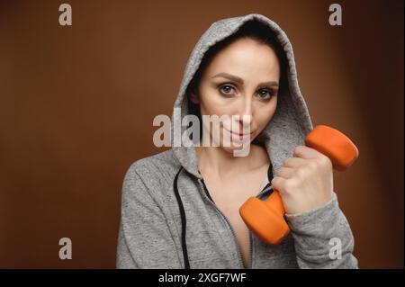 Weibliche Trainerin in einer Kapuze mit Kurzhanteln in den Händen. studio-Porträt Stockfoto