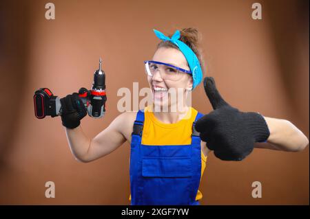 Junge lächelnde praktische Frau, die mit Schraubenzieher arbeitet und Daumen nach oben zeigt. Porträt eines Baumeisters oder Handwerkers mit einem Schraubenzieher in der Hand Stockfoto