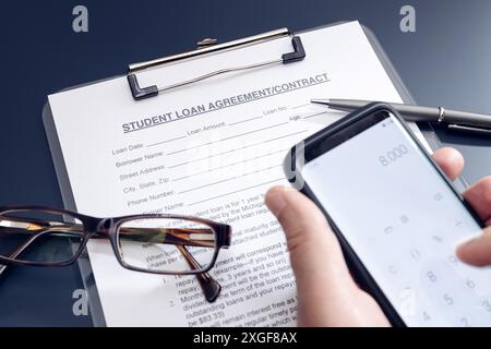 Blank Student Loan Antrag auf Tisch und Hand halten ein Smartphone mit Rechner-App. Bildungskosten Stockfoto