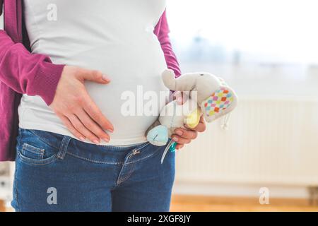 Nahaufnahme einer jungen Mutter, die ein Plüschspielzeug auf ihrem schwanger, kaukasischen Bauch hält Stockfoto