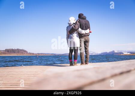 Das junge Paar steht auf einem Steg und genießt den Blick über den See, Winterzeit Stockfoto