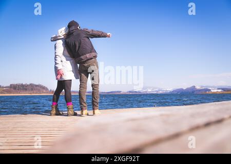 Das junge Paar steht auf einem Steg und genießt den Blick über den See, Winterzeit Stockfoto