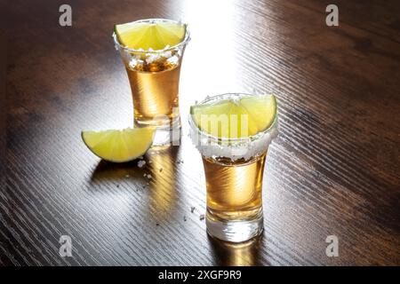 Tequila-Shots mit salzigen Rändern und Limettenscheiben auf hölzernem Hintergrund Stockfoto