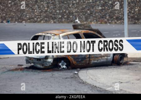 Das Auto wurde von einem Pyromanen mit einem Polizeiband verbrannt, auf dem steht: "Polizeilinie nicht überkreuzen". Stockfoto