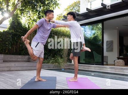 Yoga praktizieren, männliches schwules Paar, das draußen auf Yogamatten auf einem Bein balanciert Stockfoto