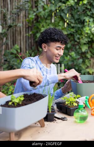 Gartenarbeit zu Hause, junger Mann pflanzt Setzlinge in Töpfen, lächelt und genießt Stockfoto