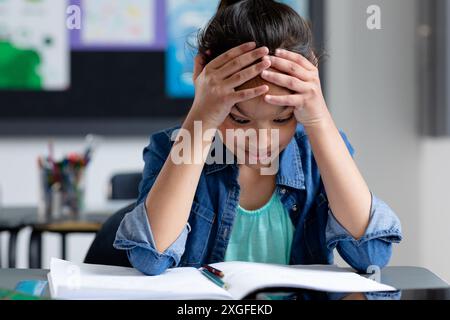 Gestresstes birassisches Schulmädchen sitzt im Unterricht am Schreibtisch, Kopf in Händen, starrt auf Buch, Kopierraum Stockfoto