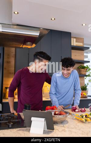 Zusammen kochen, männliches Schwulenpaar, das Gemüse in der modernen Küche mit Tablette zubereitet Stockfoto