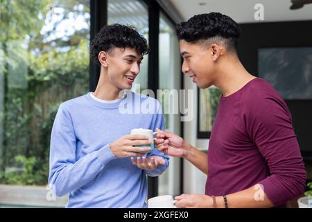 Lächelndes männliches Schwulenpaar, das gemeinsam Kaffee in gemütlicher Atmosphäre genießt Stockfoto