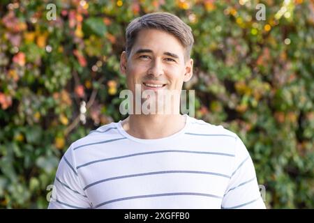 Lächelnder Mann in gestreiftem Hemd, der draußen steht, mit Grün im Hintergrund Stockfoto
